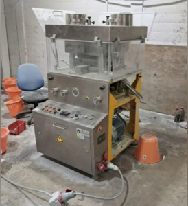 industrial pill press in a dusty looking concrete room